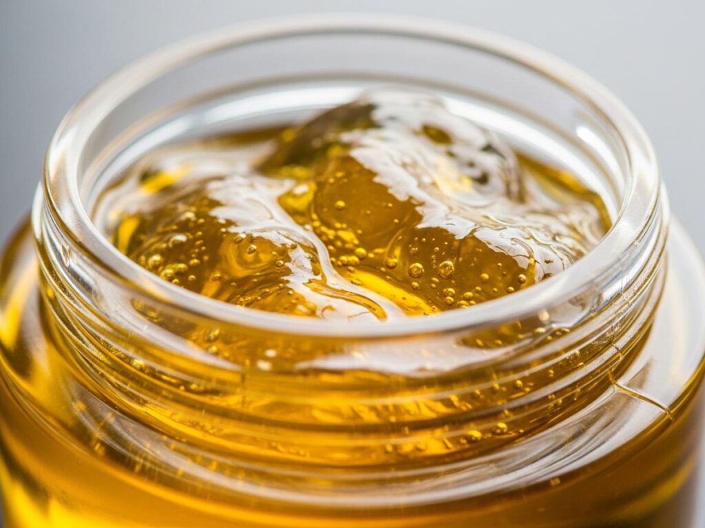 A close-up of golden hash oil in a clear container, showing its clarity and texture.